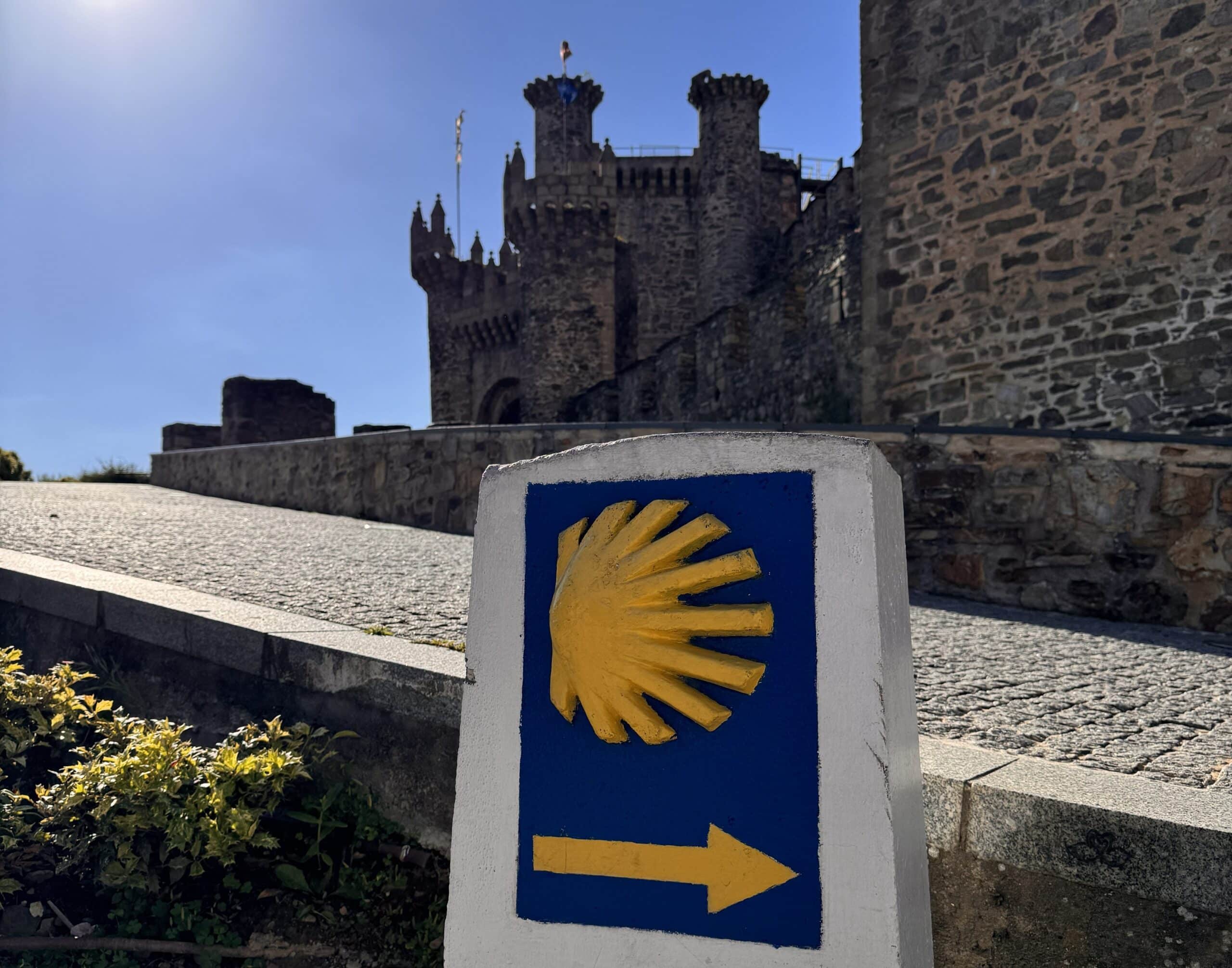 Mojón del Camino de Santiago con la concha y la flecha amarilla frente al Castillo de los Templarios de Ponferrada
